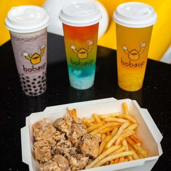 Three Boba Up drinks and a box of fried chicken and french fries on a black surface.