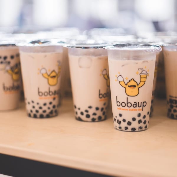 Multiple Boba Up bubble tea cups with the brand's logo and tapioca pearls on a wooden surface.